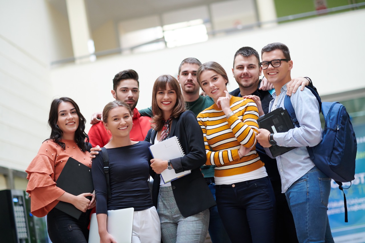a group of students with books, a laptop and smartphones talk in a modern college